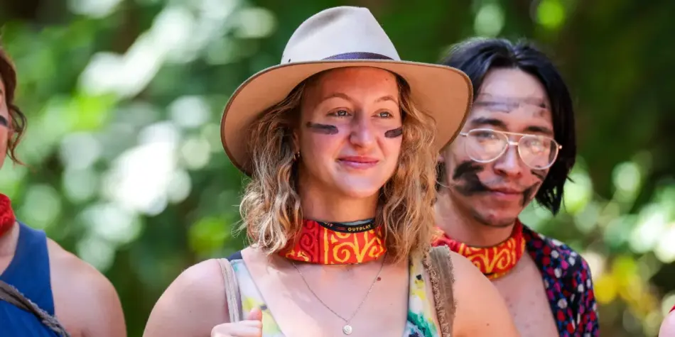 Ally Kettle from Australian Survivor 2025, wearing a wide-brimmed hat and tribal buff, smiles with face paint in a jungle setting.