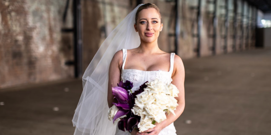 Jamie Marinos poses in a white wedding gown, holding a bouquet of white and deep purple flowers on Married at First Sight (MAFS) 2025.