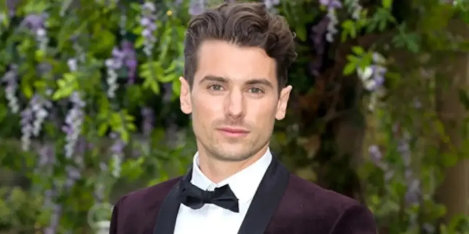 Matty J in a tuxedo, posing outdoors with greenery and purple flowers in the background