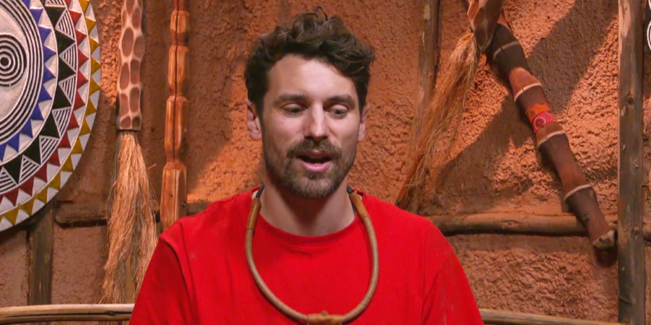 Matty J on I'm a Celebrity 2025 wearing a red shirt and wooden necklace, speaking in the Tok Tokkie