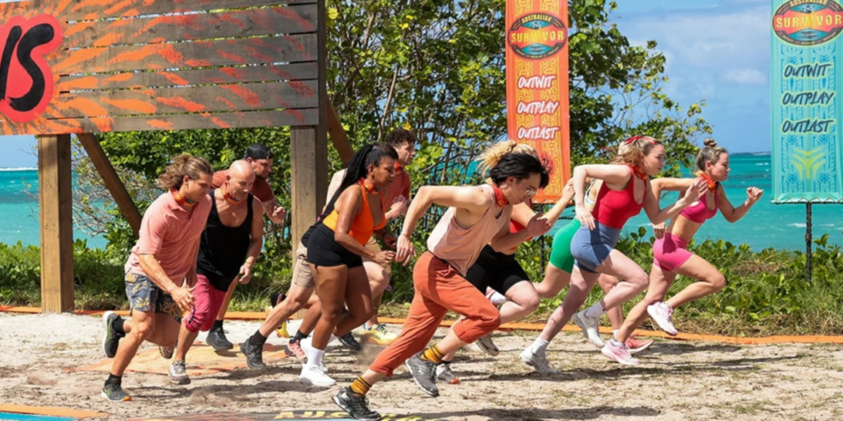 Myles Kuah and his Brains tribe members, all wearing red buffs, sprint forward at the start of a challenge on Australian Survivor 2025, with a tropical backdrop of blue ocean and lush greenery