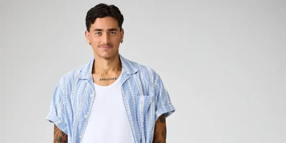 Promotional image of Bernie from Love Triangle Season 3 (2025), wearing a casual blue patterned short-sleeve shirt over a white tank top, smiling confidently against a neutral backdrop