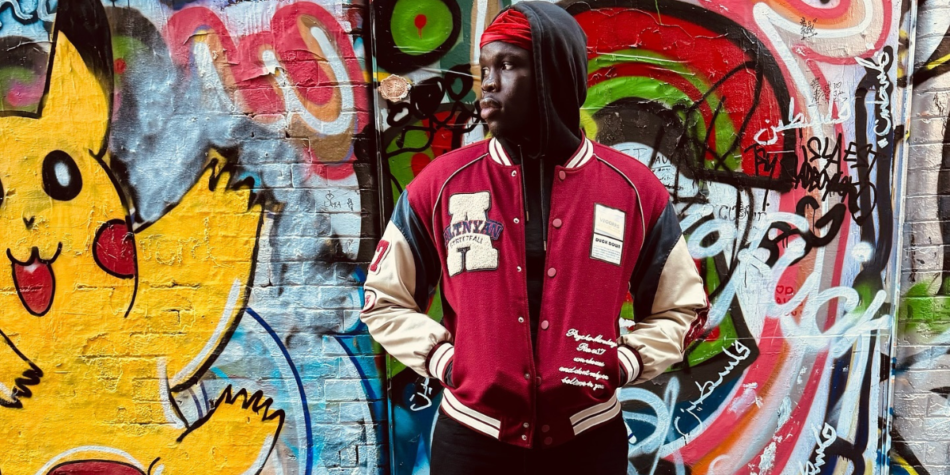 Bony Onyango from Australian Idol 2025 posing against a vibrant graffiti wall, wearing a red varsity jacket, black hoodie, and red headband.